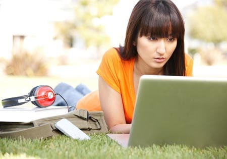 A young woman works on her laptop outside