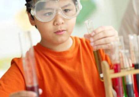 Boy wearing goggles holding test tubes.