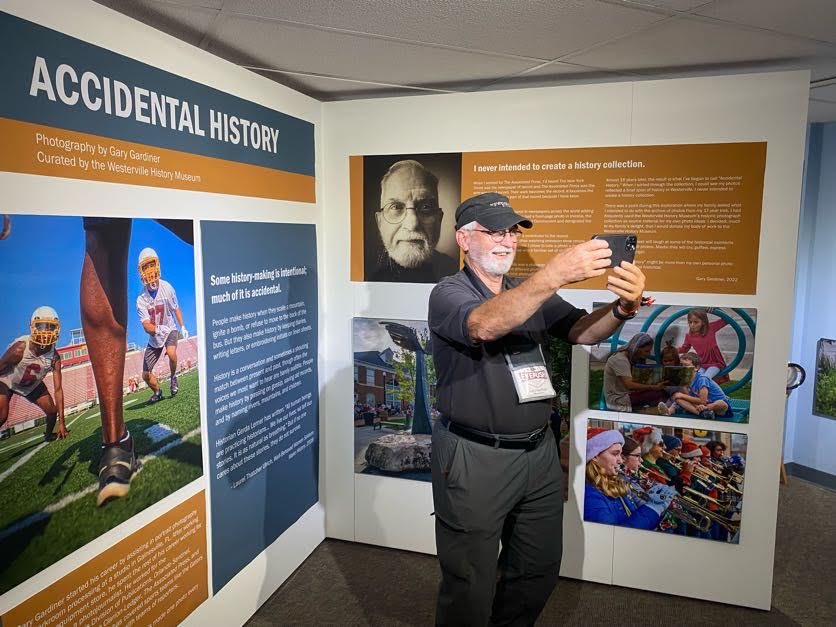 Photo of photographer and “accidental historian”, Gary Gardiner, taking a selfie with the exhibit featuring his work