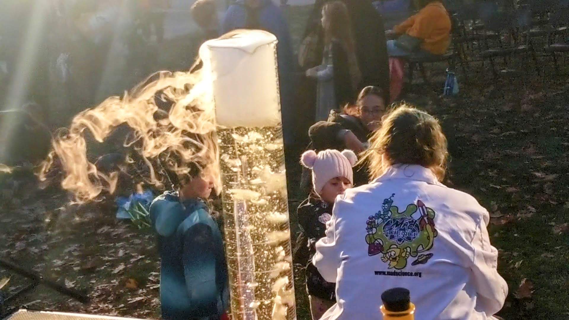 Photo of presenter from Mad Science of Northeast Ohio talking to children with a glass cylinder of bubbling liquid in the foreground
