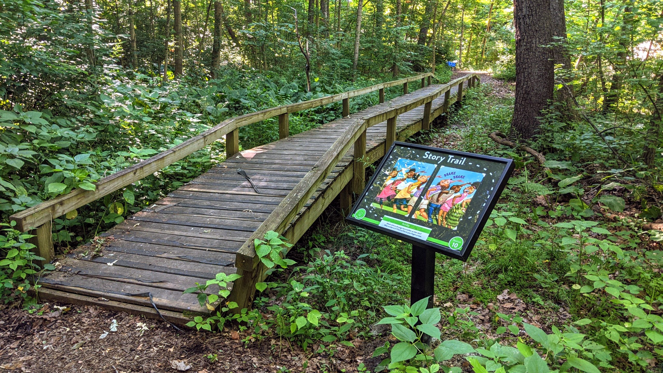 Photo of a story trail post displaying a book page from I Got the Rhythm by Connie Schofield-Morrison along a wooded path at Ridgewood Park in Blendon Township
